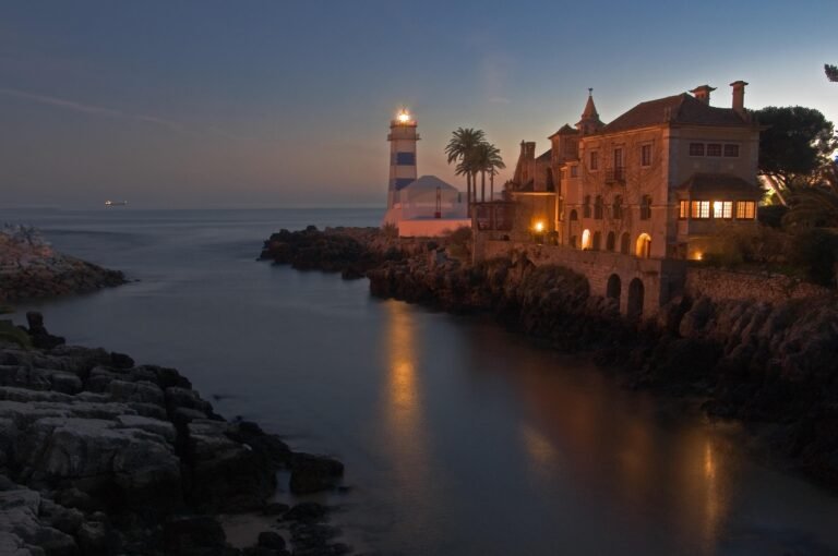 The Santa Marta lighthouse and a seafront mansion on the rocks in Cascais at dusk