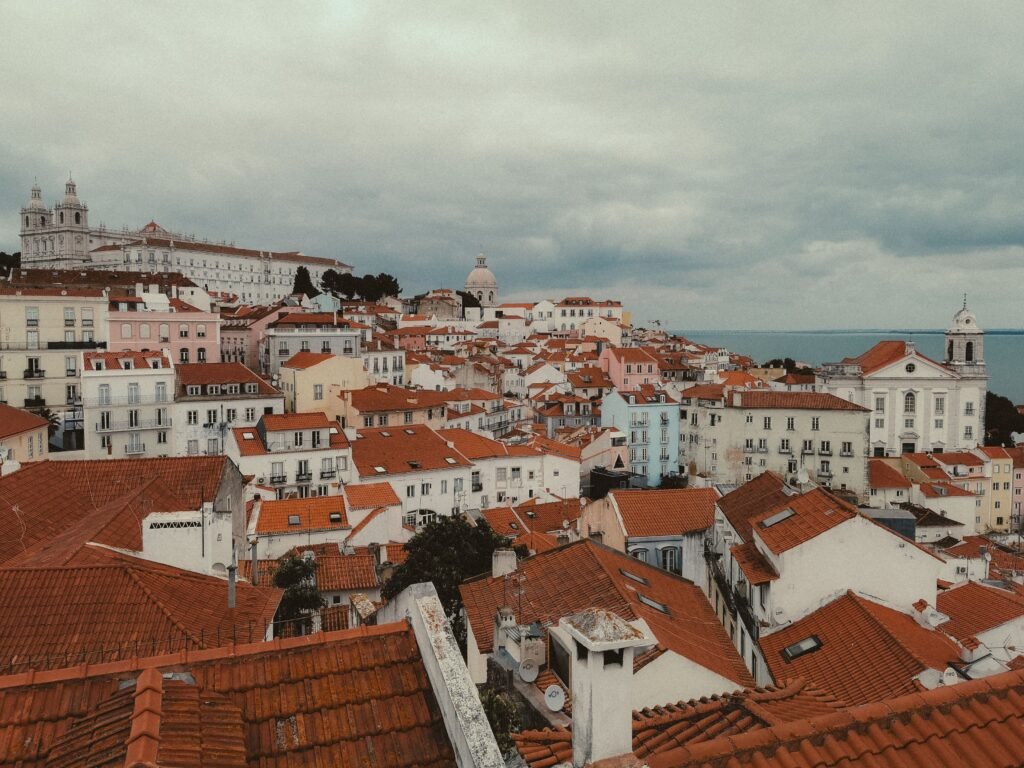 The terracotta rooftops of Alfama running down to the river, with S&atilde;o Vicente de Fora and the dome of the National Pantheon, seen from a Lisbon miradouro