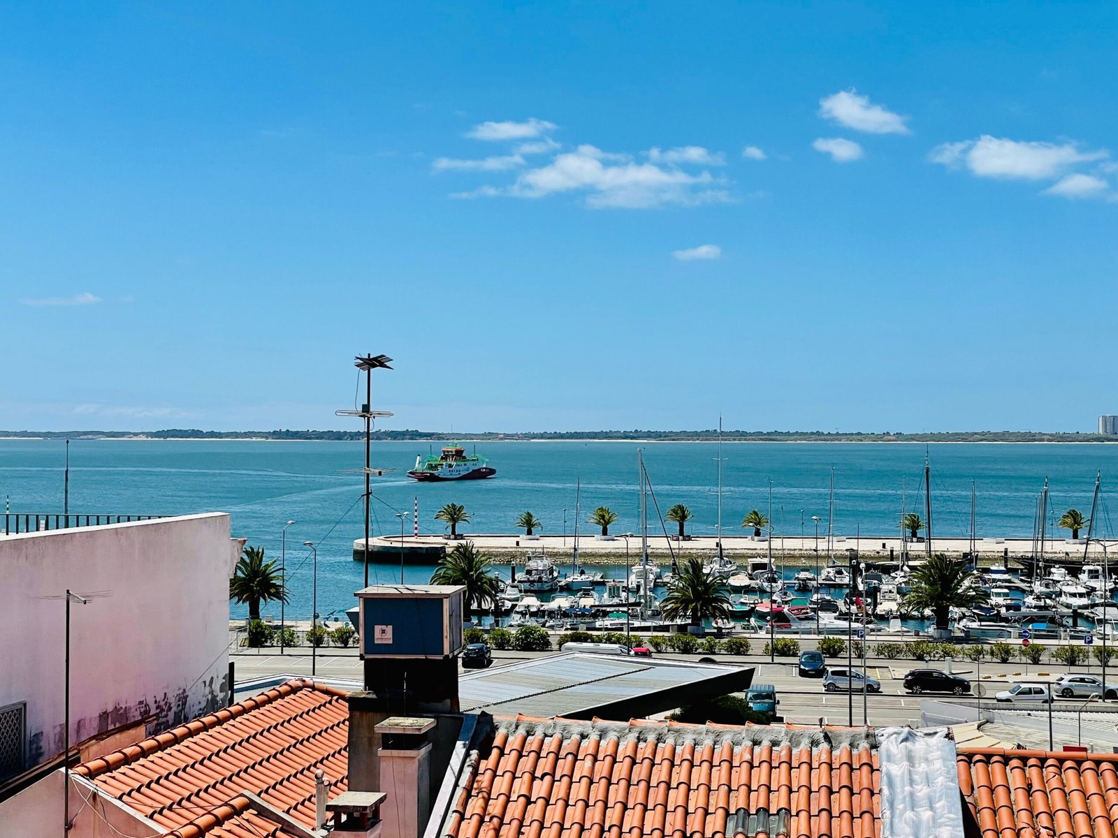 A picturesque view of Setúbal Marina with boats, rooftops, and the sea under a blue sky.