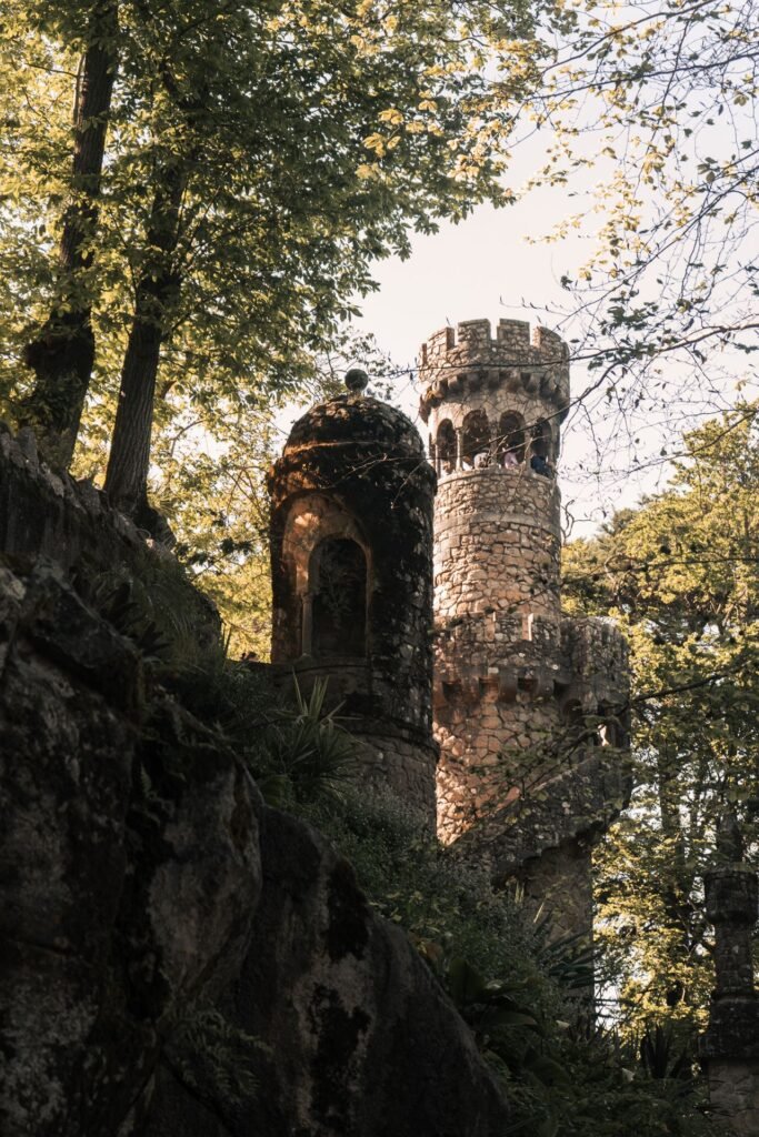 A crenellated stone tower rising above the forest gardens of Quinta da Regaleira in Sintra